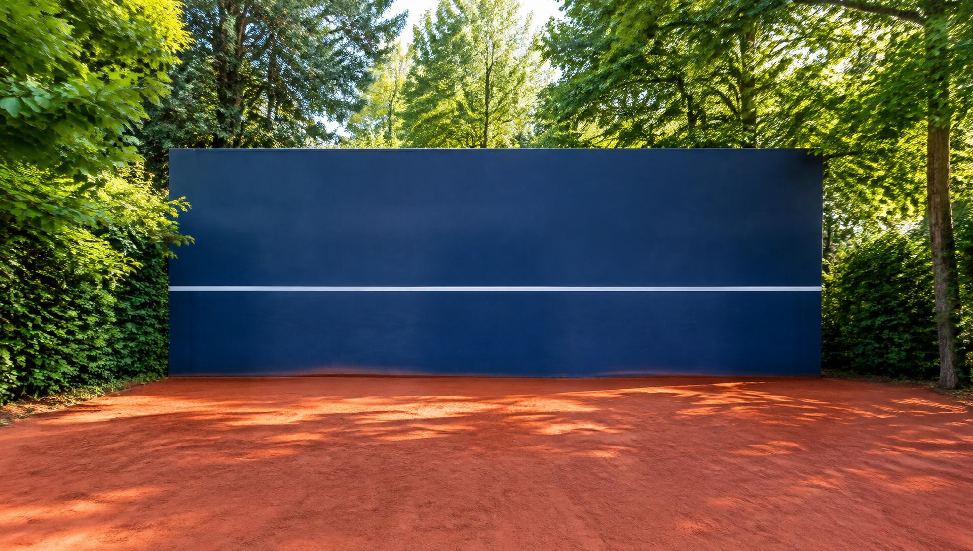 Mur d'entraînement de tennis bleu sur court en terre battue, entouré d'arbres feuillus avec une seule ligne blanche horizontale